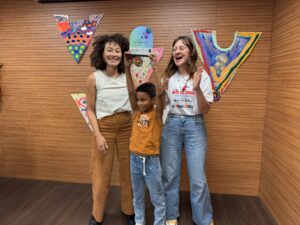 No centro da foto, Wagner Luan ergue o troféu com duas mãos. Camila e Laura estão ao lado dele e comemoram a premiação.